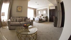 A spacious living room with a sofa, a glass coffee table with fruit, and a dining area with a chair. - Lumiere Des Etoile (Salmiya)