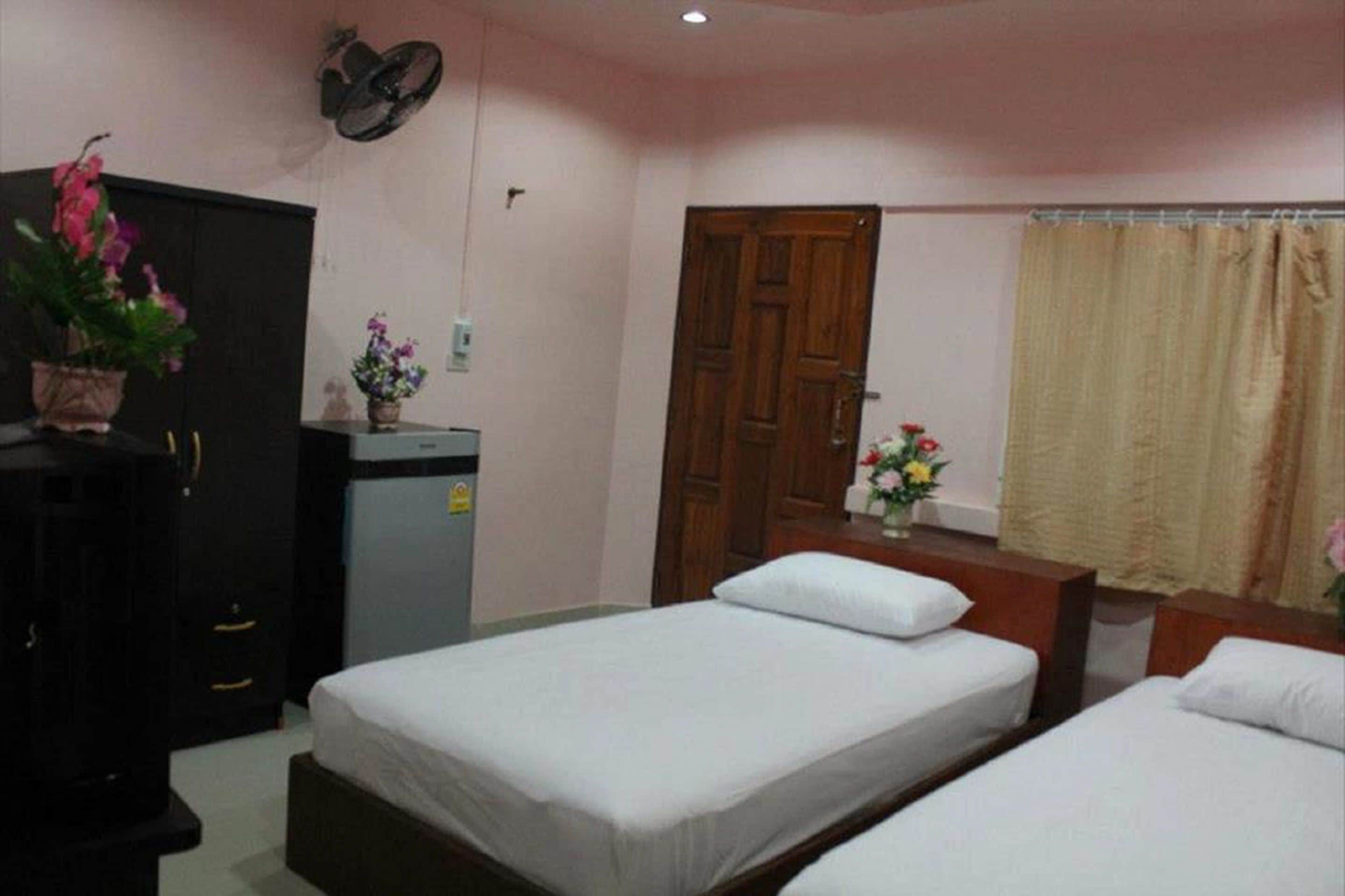 A bedroom with two single beds, a wooden wardrobe, a desk with a chair, and a wall-mounted fan.