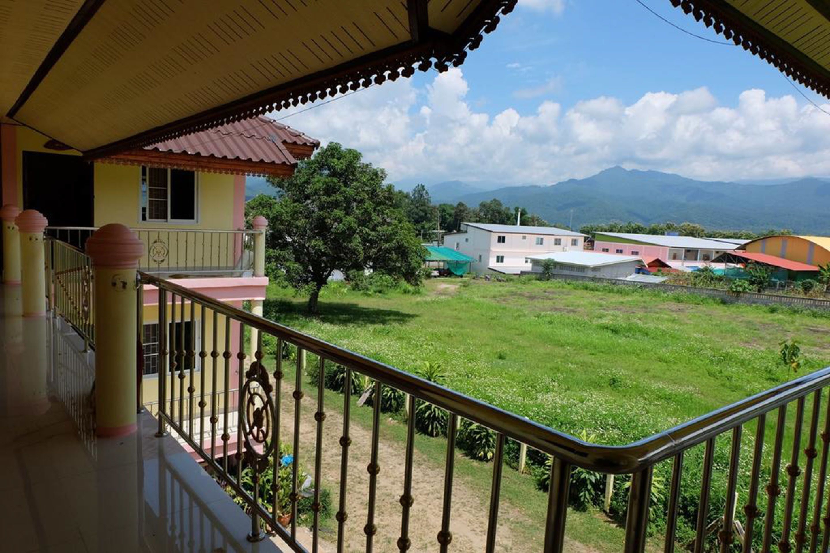 A balcony with a view of a green field, a tree, and buildings in the distance.