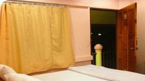 Un lit simple avec un matelas et un oreiller blancs, un rideau jaune et une porte en bois.