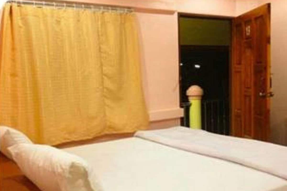 A single bed with a white mattress and pillow, a yellow curtain, and a wooden door.