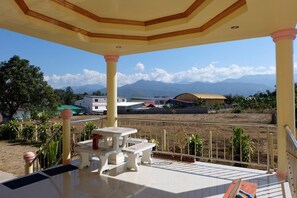 A covered outdoor area with a table and benches, overlooking a landscape with buildings and mountains. - Nakorn Nan Apartment (Pua)