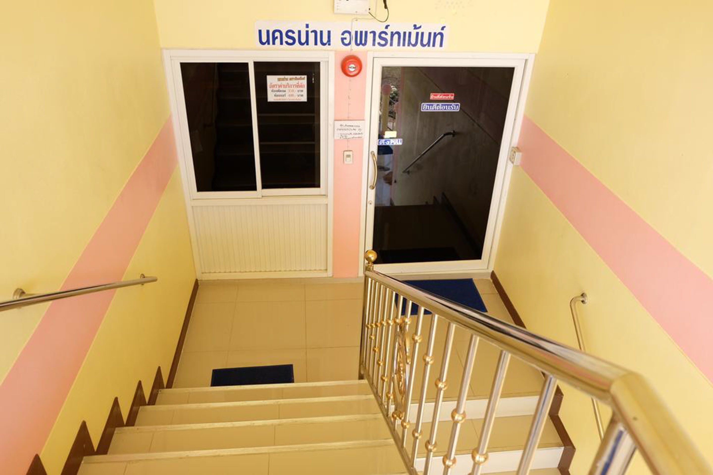 Una escalera con barandilla, una puerta con letrero y una pared con indicación de dirección.