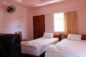 Una habitación con dos camas individuales, una puerta de madera, una ventana con cortinas y un ventilador.