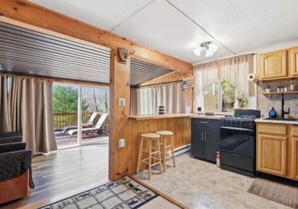 A kitchen with wooden cabinets, a black stove, and a bar area with stools. - Pocono private retreat (East Stroudsburg)