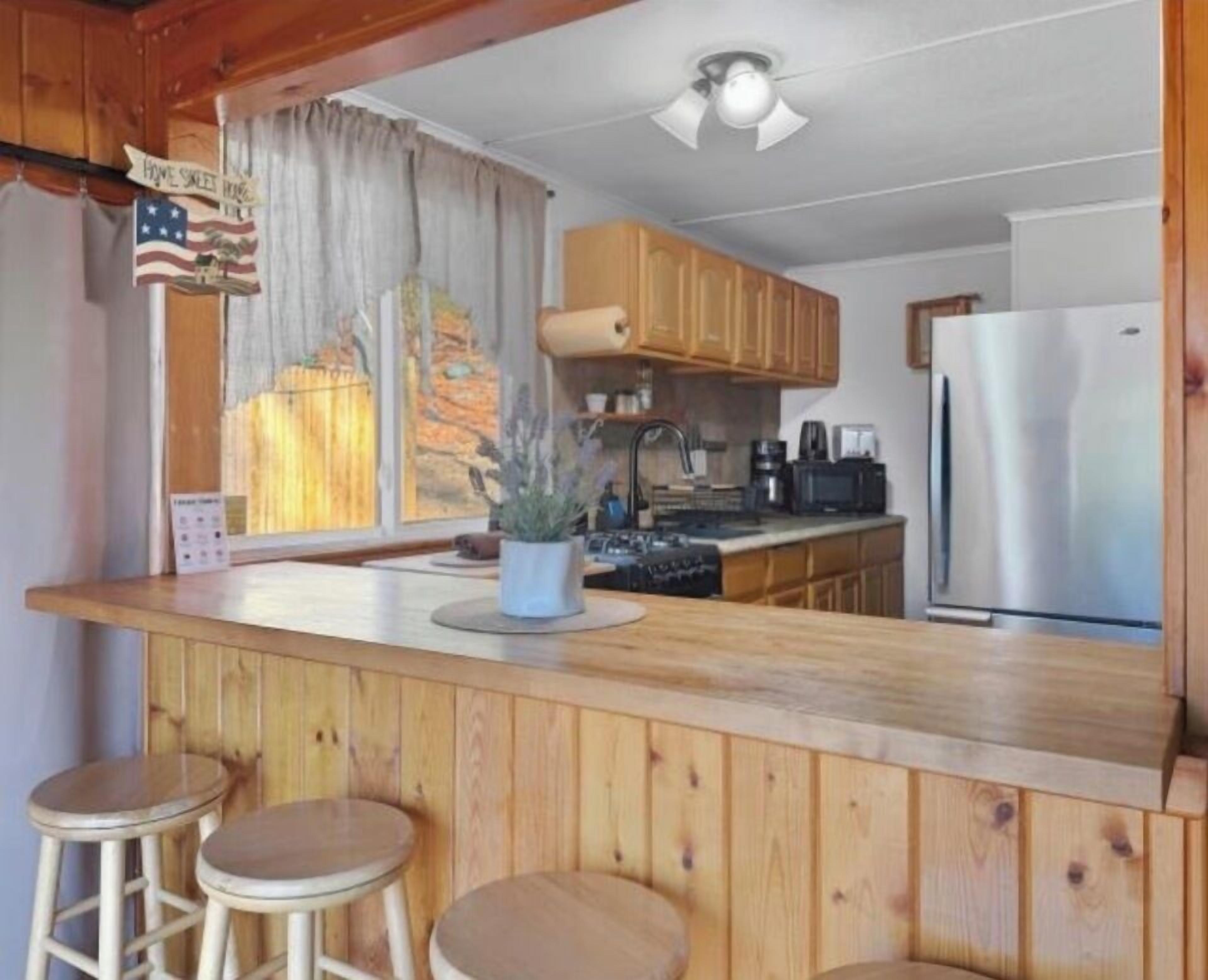 A kitchen with wooden cabinets, a stainless steel refrigerator, a sink, and a bar area with stools.