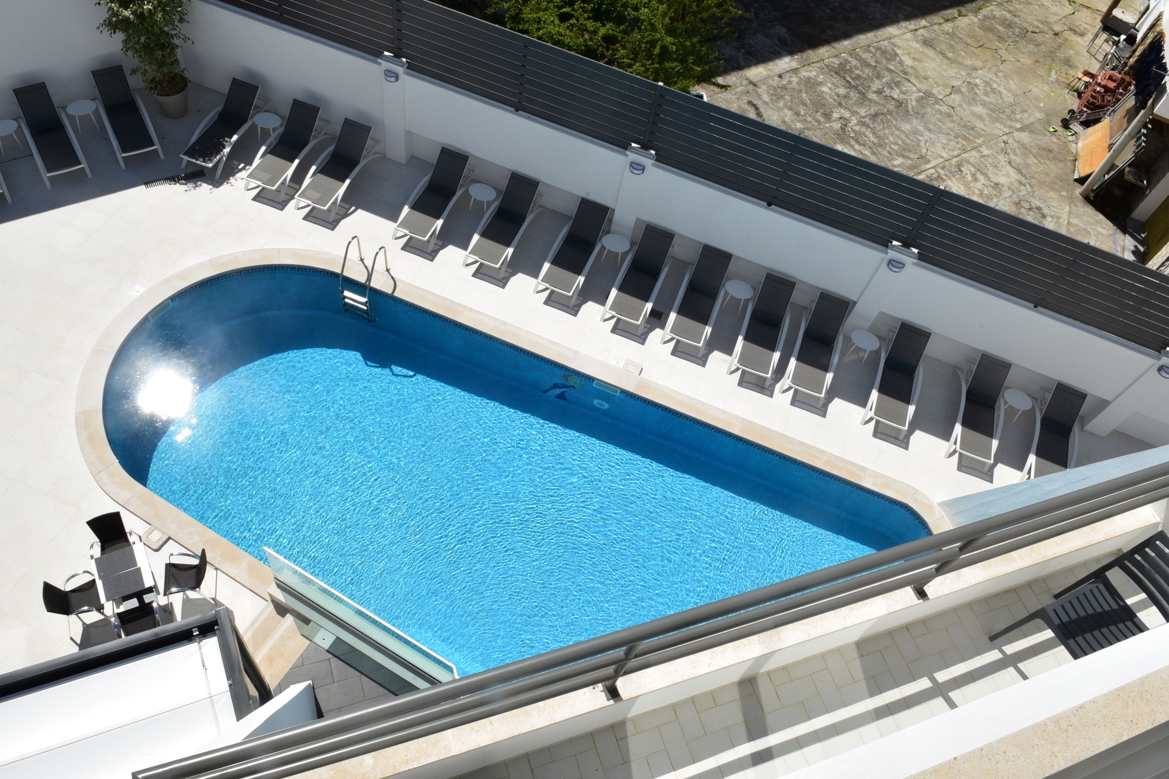 A rooftop swimming pool with sun loungers and a small table.