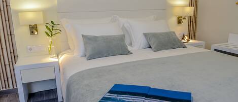Una cama bien hecha con sábanas blancas y dos almohadas grises, una mesita de noche con lámpara y una pared con estampado de bambú.