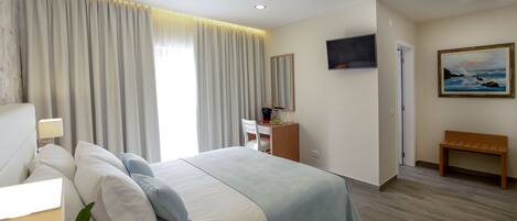A hotel room with a large bed, a desk, a chair, a TV, and a painting on the wall.