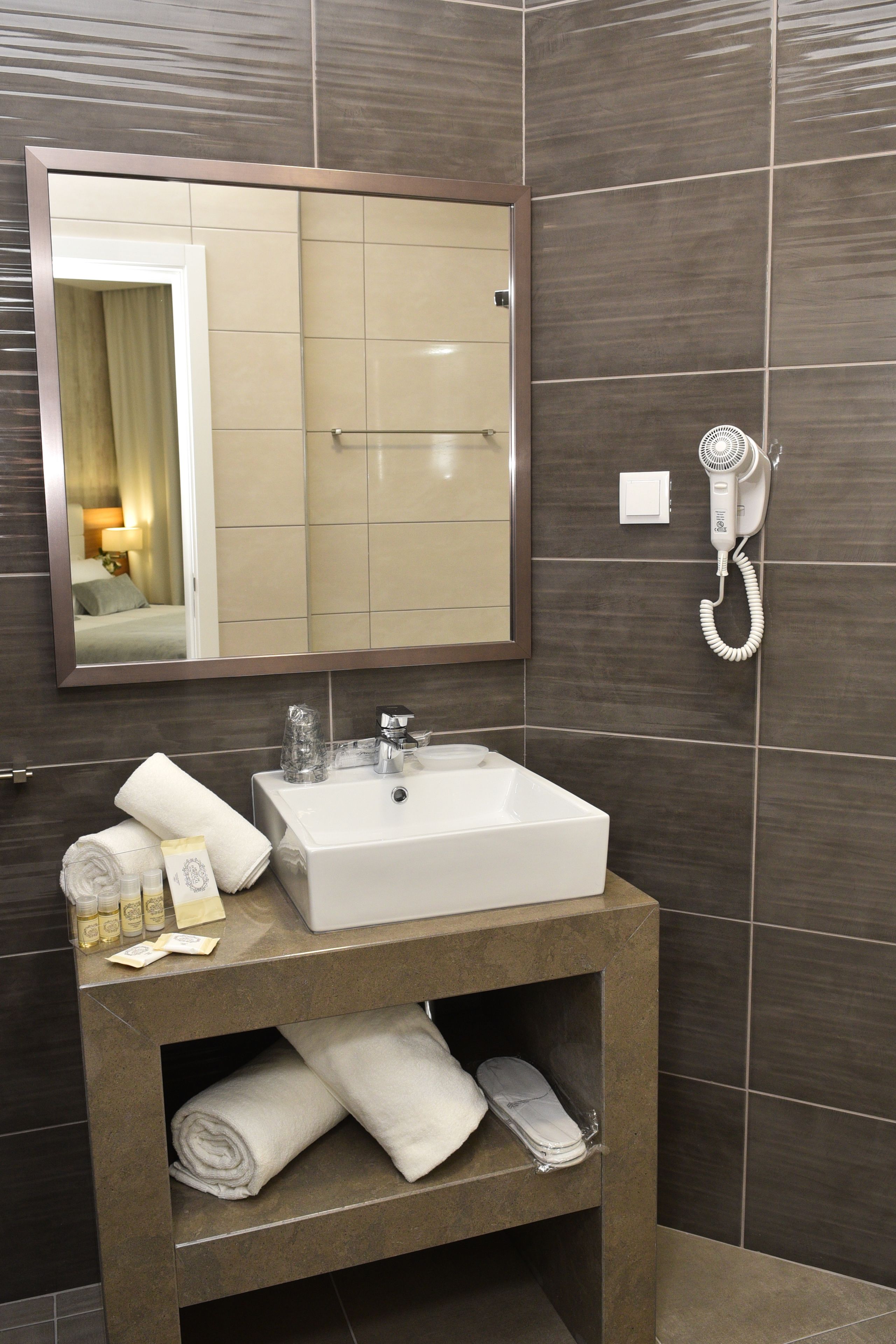 Une salle de bain avec un lavabo blanc, un miroir et un sèche-cheveux fixé au mur.
