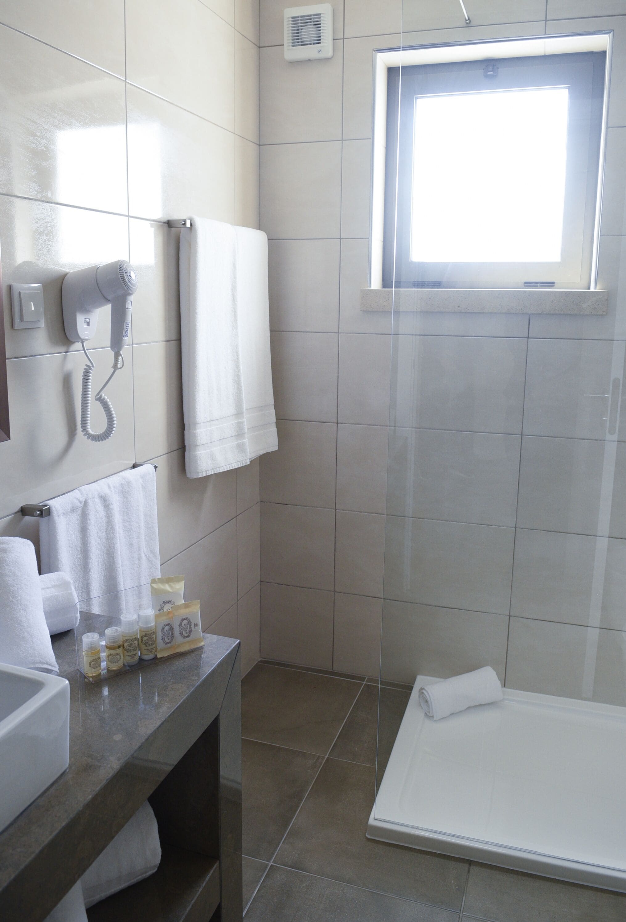 A bathroom with a sink, a hairdryer, a towel rack, and a window.