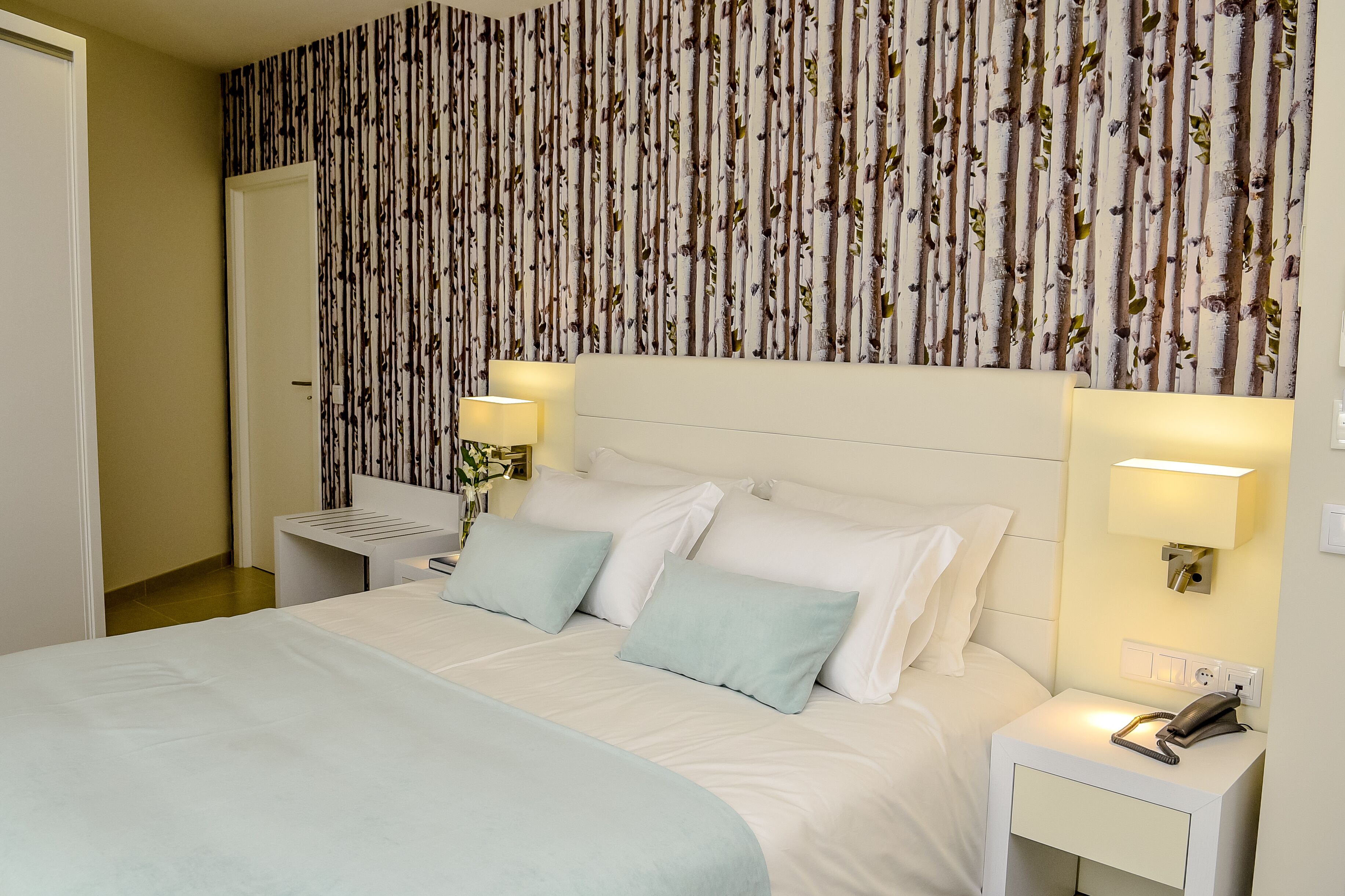 Una habitación de hotel con una cama, dos mesitas de noche y una pared a rayas verticales.