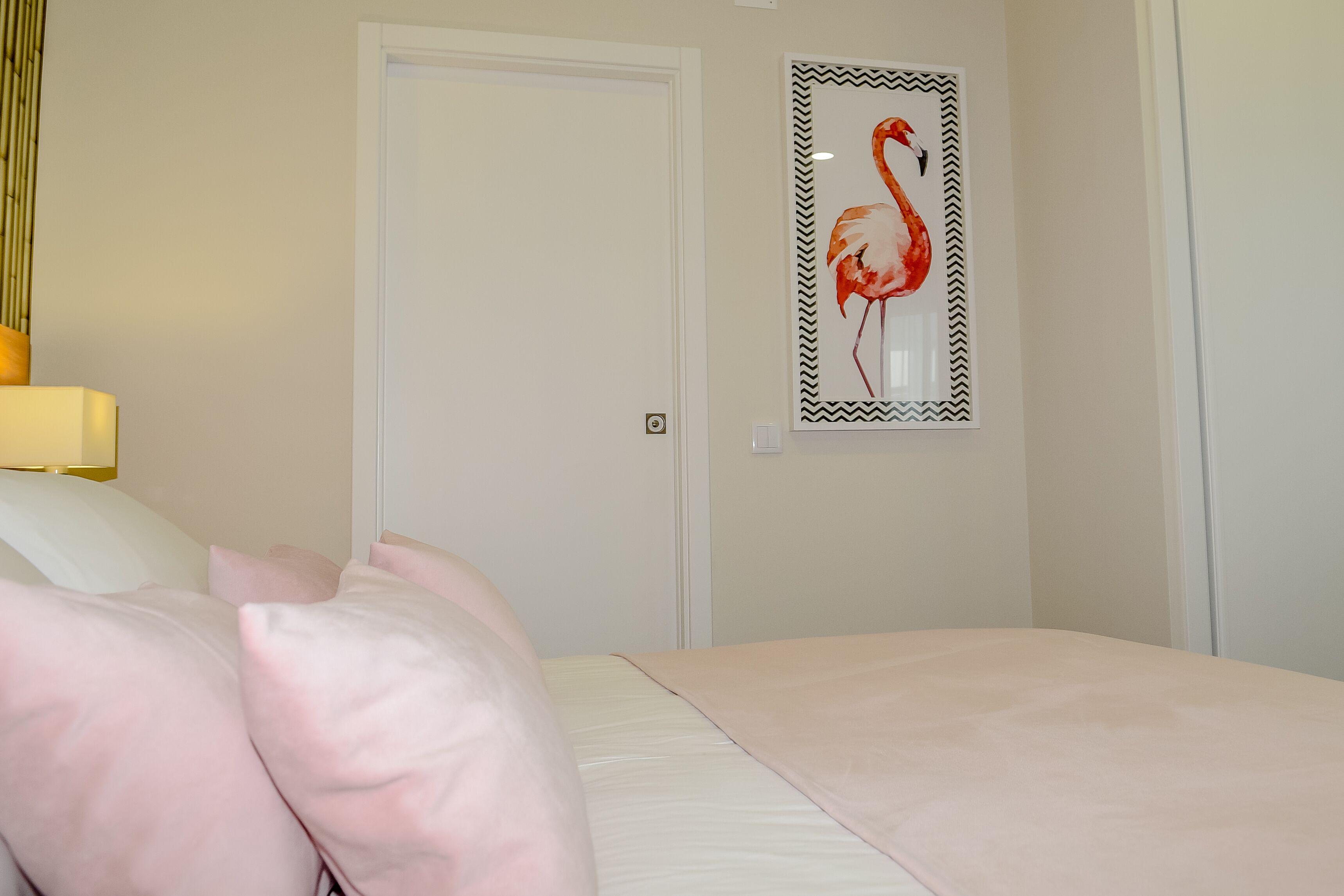 Une chambre d’hôtel avec un lit, une porte et un tableau représentant un flamant rose accroché au mur.