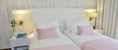 Une chambre d’hôtel avec deux lits, du linge de lit blanc et des lampes de chevet.