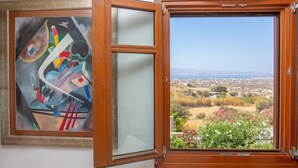 Een kamer met een groot abstract schilderij aan de muur en een raam met uitzicht op een landschap.