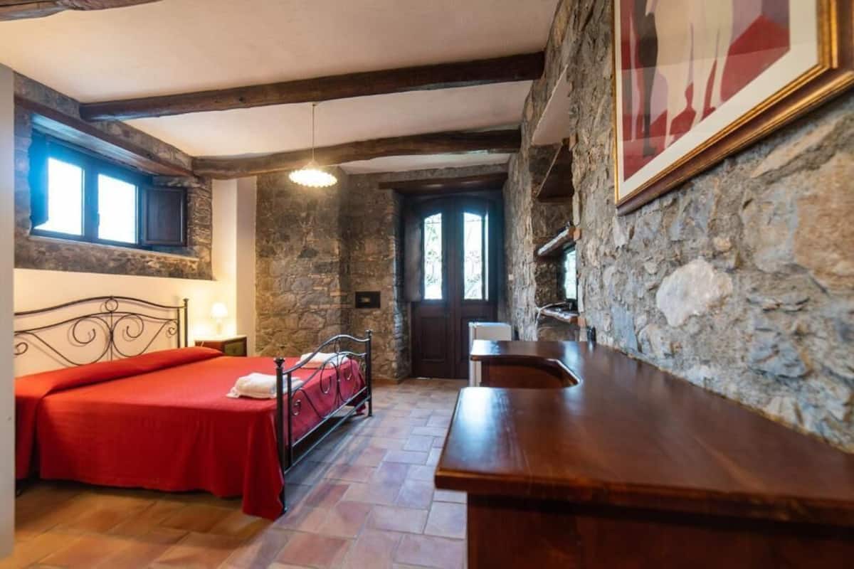 Une chambre avec un mur en pierre, un lit en bois, une table de chevet et une fenêtre.