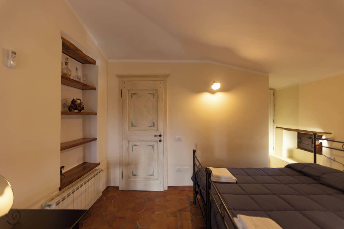 Une chambre à coucher avec un lit, un radiateur, des étagères, une porte et un luminaire fixé au mur.