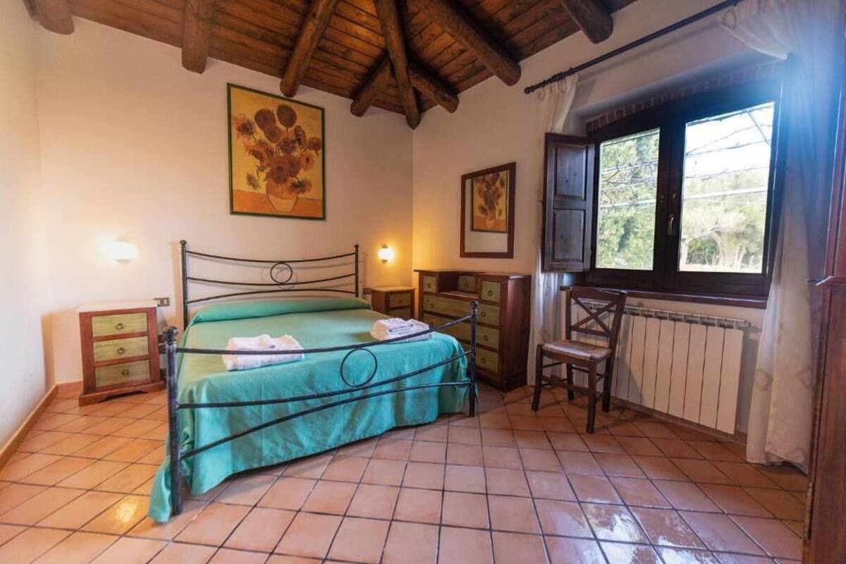 Une chambre à coucher avec un lit, une chaise en bois, une commode et une fenêtre avec des rideaux.
