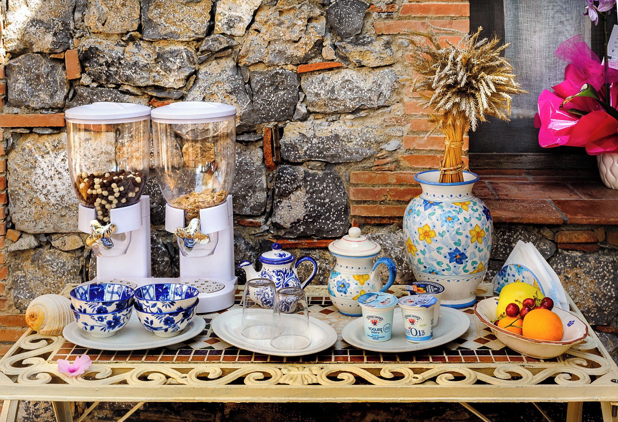 A table with various kitchenware, including a coffee grinder, teapots, and bowls, set against a stone wall.