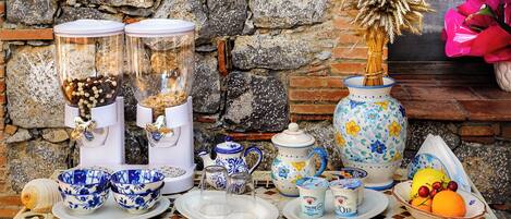 A table with various kitchenware, including a coffee grinder, teapots, and bowls, set against a stone wall.