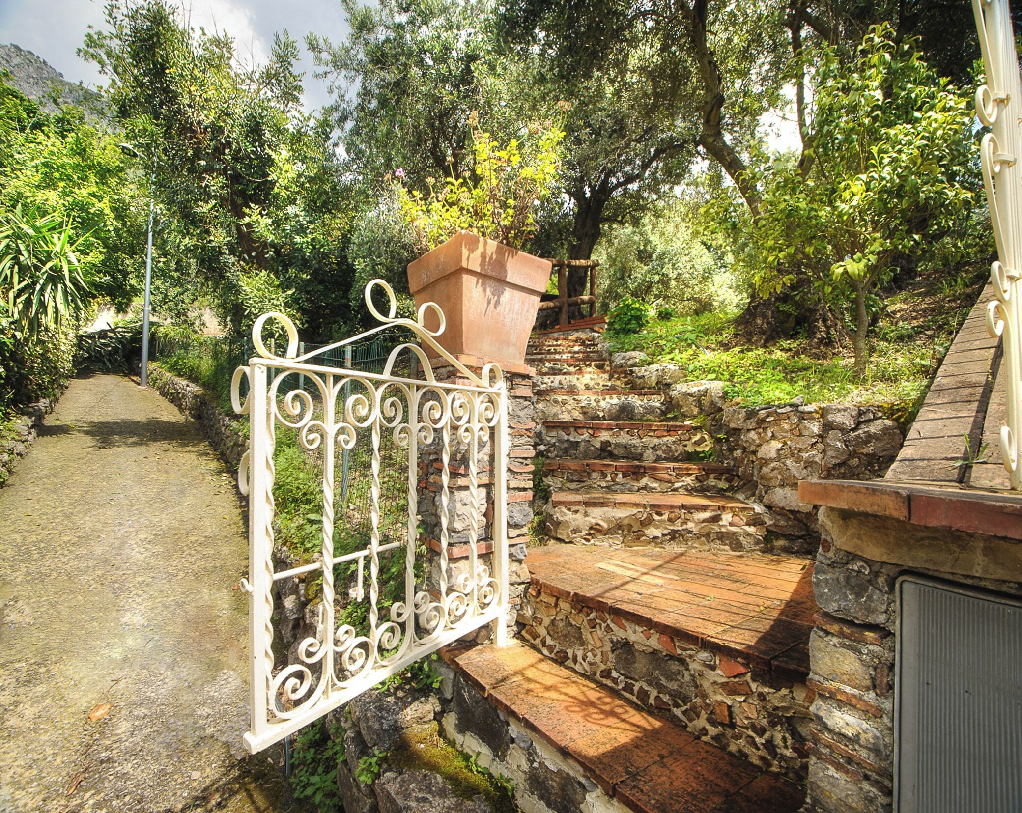 Una escalera de piedra que sube hacia una casa con un portón de metal.