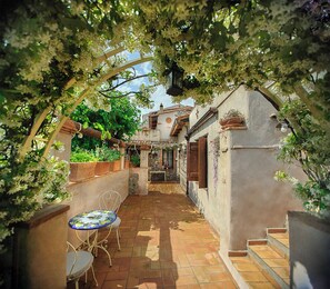 A covered patio with a table and chairs, a stone wall, and a view of a building in the background. - B&B La Torretta (Maratea)