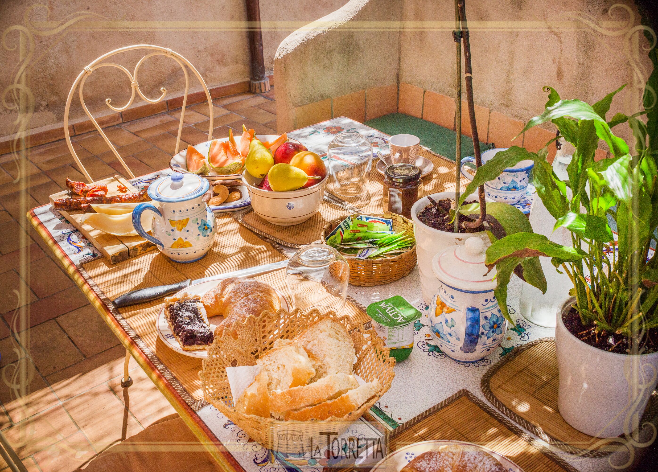 Una mesa de desayuno con diversos alimentos, una tetera y una planta en maceta.