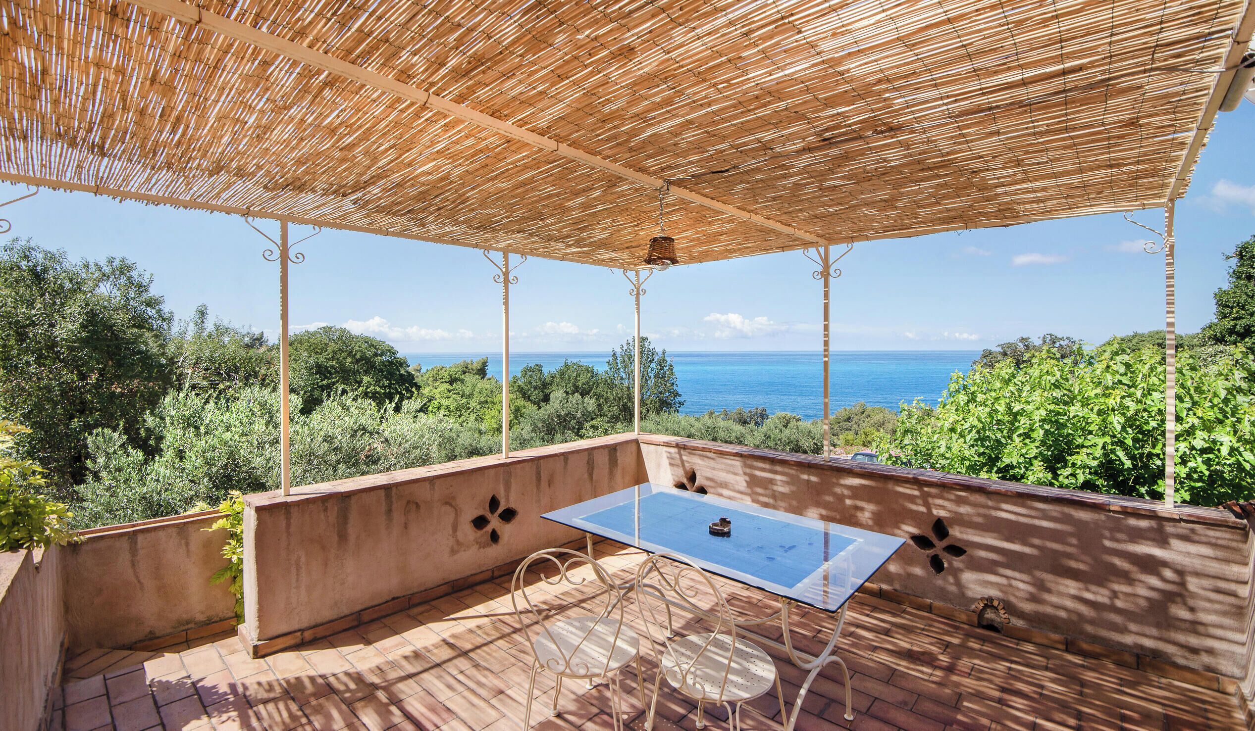 Un área de estar al aire libre con una mesa y sillas, una pérgola arriba y vista al mar.
