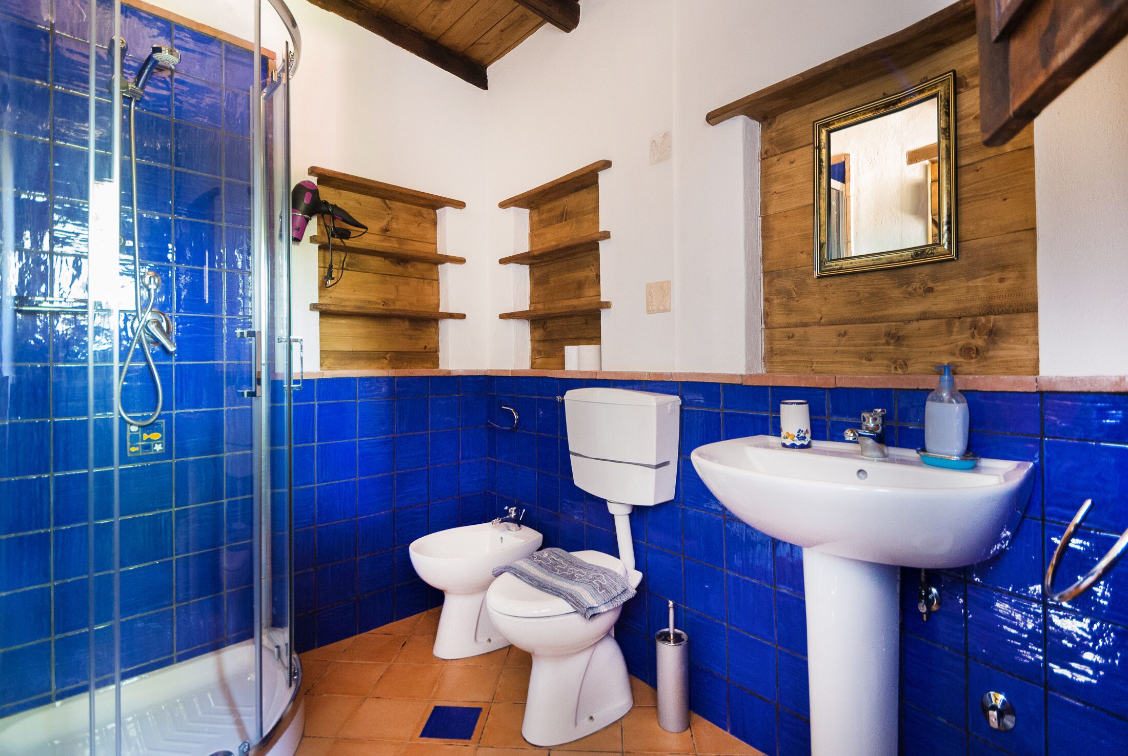 Un bagno con piastrelle blu, una doccia, un water, un bidet e un lavandino.