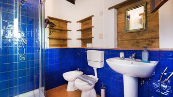 Un bagno con piastrelle blu, una doccia, un water, un bidet e un lavandino.