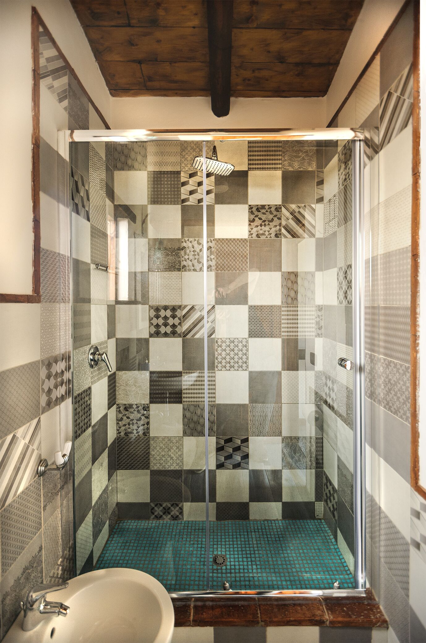 A shower with a glass door, checkered tile walls, and a sink with a white basin.