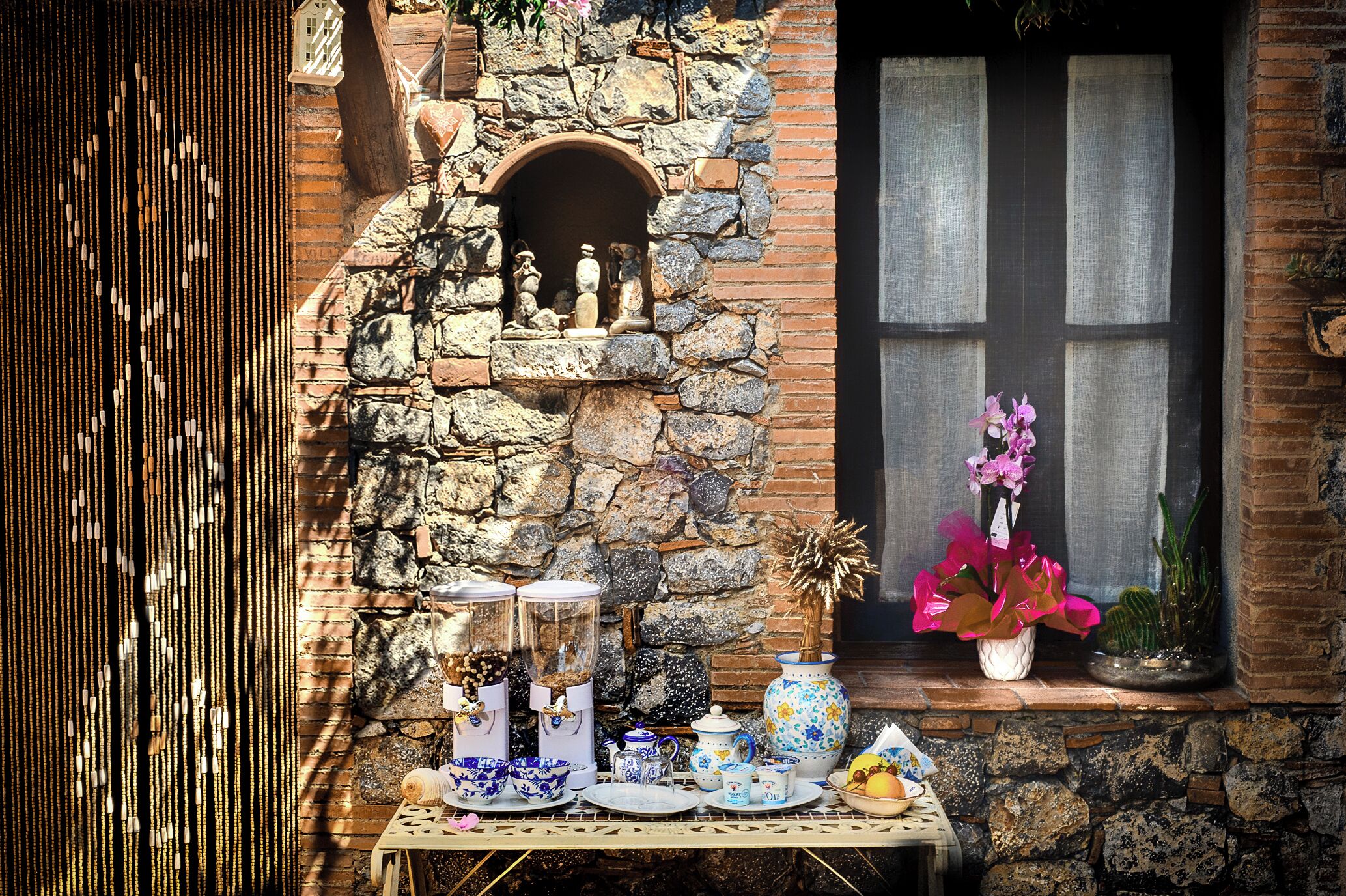 Una pared de piedra con una ventana, una mesa con varios objetos y un estante pequeño con figuritas.