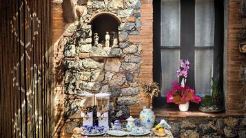 Un mur de pierre avec une fenêtre, une table sur laquelle se trouvent divers objets, et une petite étagère avec des figurines.