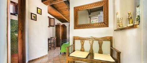 A hallway with a wooden bench, a mirror, and a shelf with decorative items.