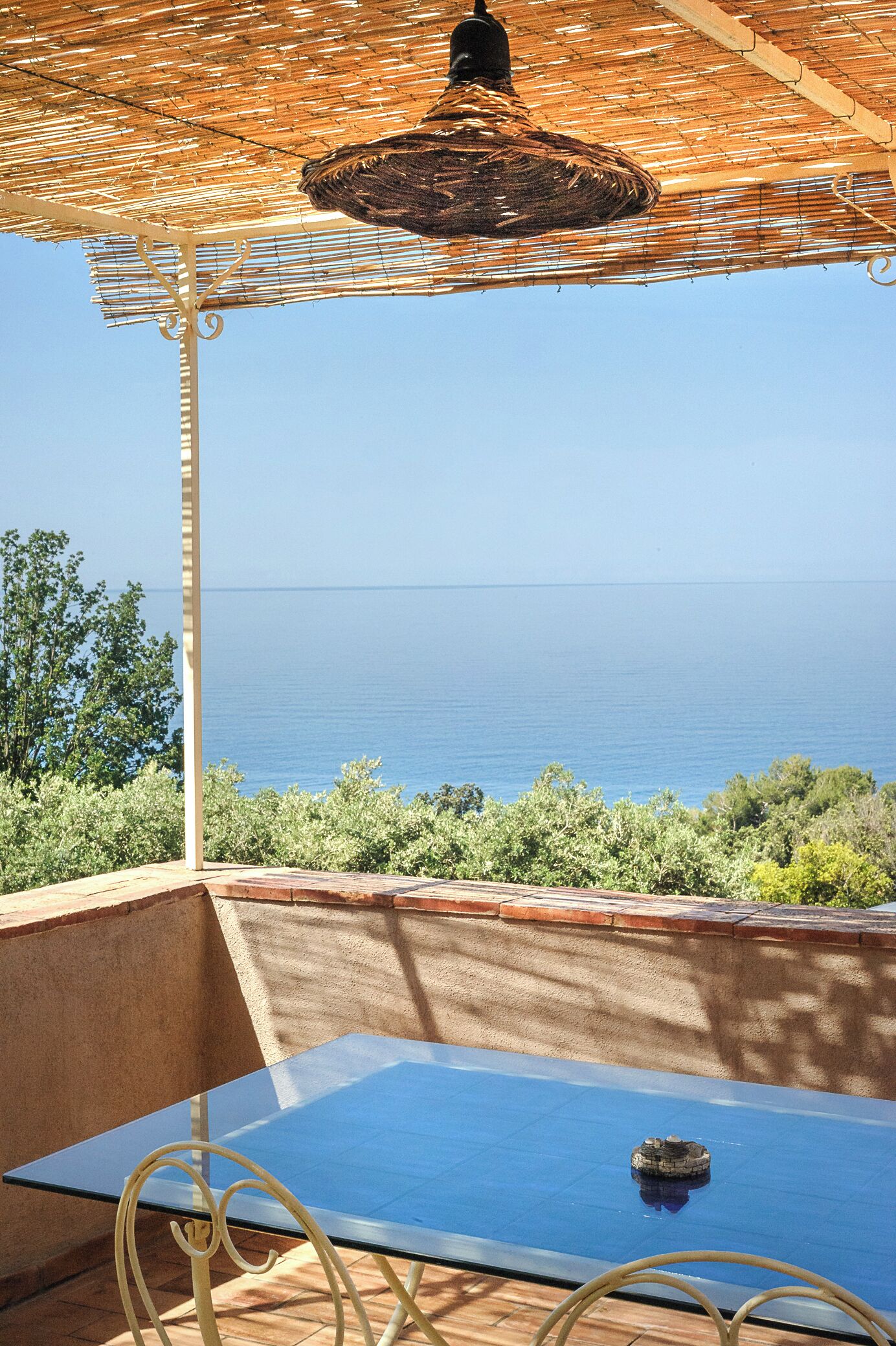 A glass table under a woven shade, overlooking a coastal landscape.