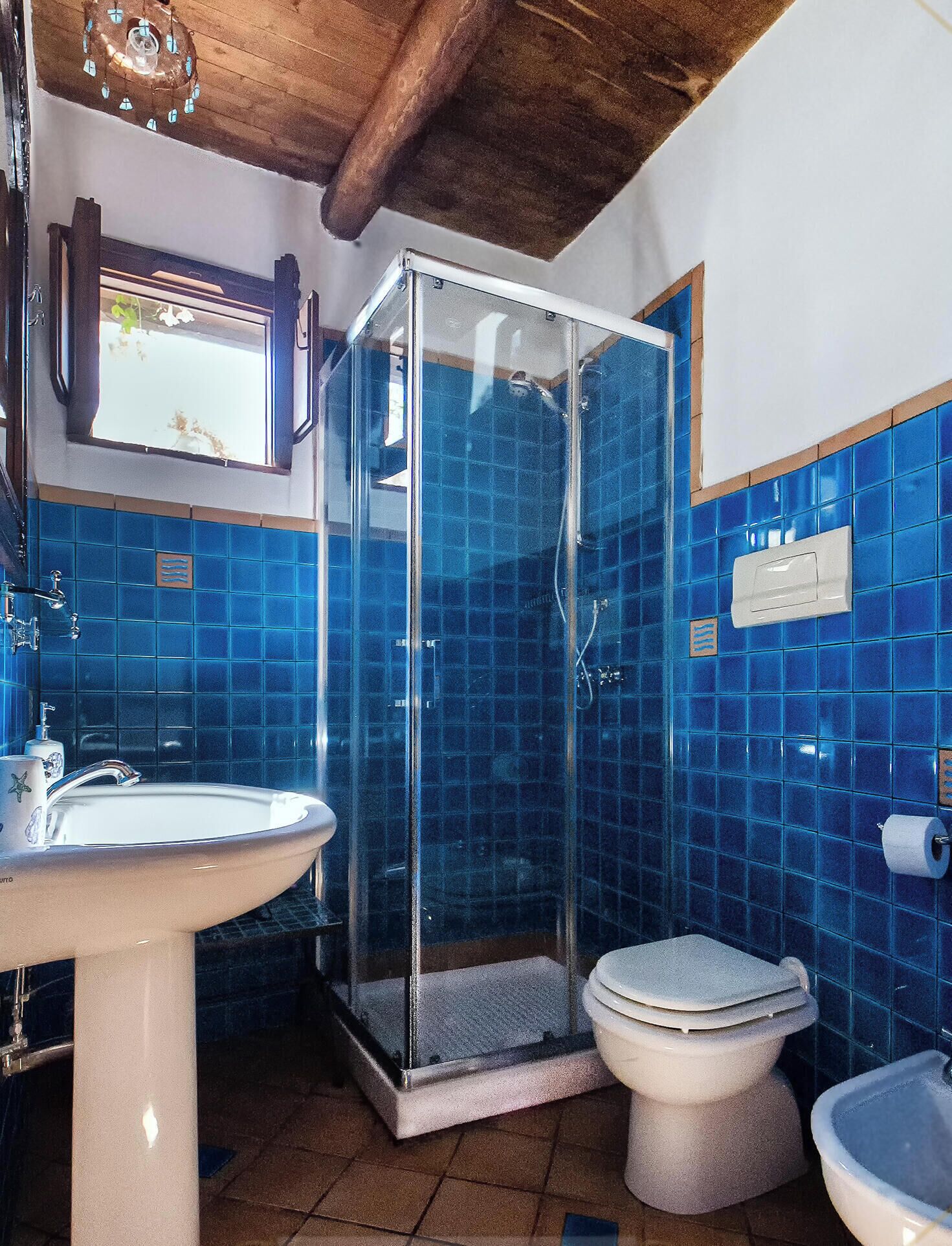 A bathroom with a glass-enclosed shower, a sink, a toilet, and blue-tiled walls.