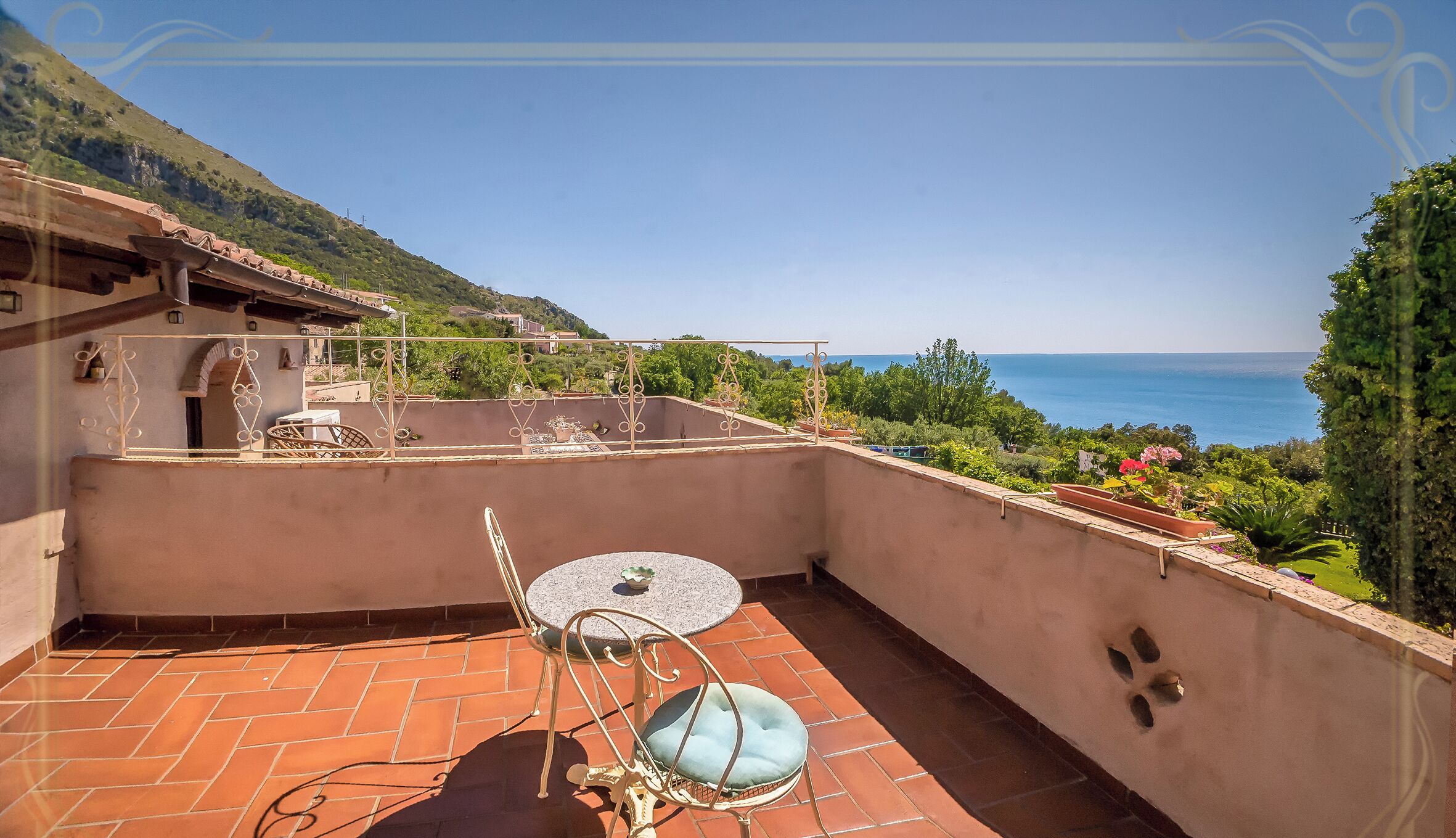 Terraço com mesa e cadeiras, com vista para a paisagem costeira.