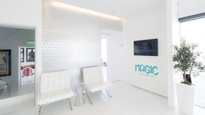 Un hall d’hôtel moderne, avec des meubles blancs, un mur orné d’un motif géométrique et un logo apposé sur le mur.