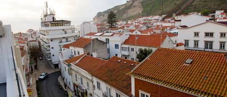 A coastal town with terracotta-tiled buildings, narrow streets, and a prominent hill in the background.