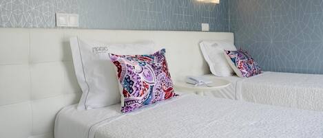 A hotel room with two beds, a white headboard, patterned wall, and two wall-mounted lights.