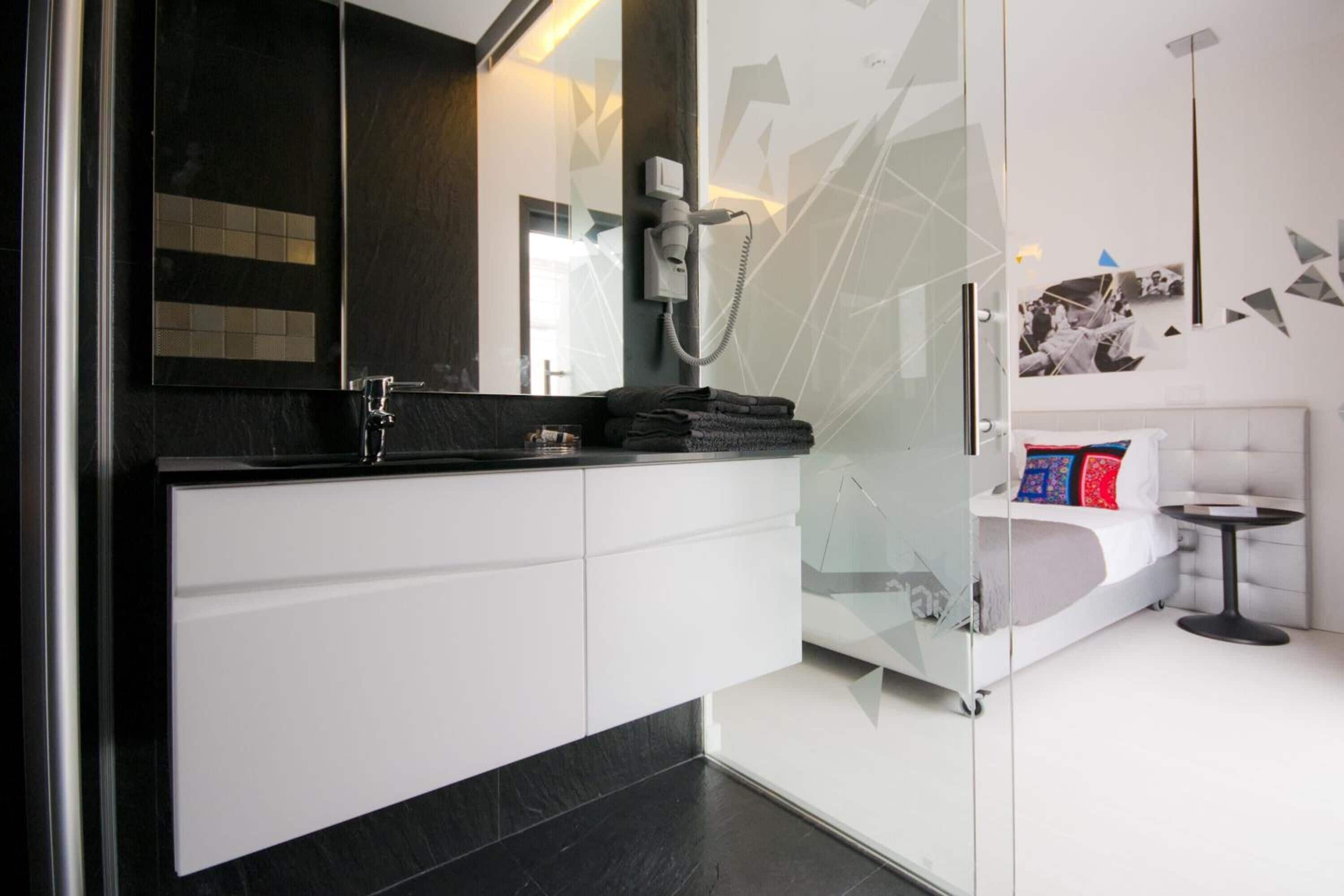 A modern bathroom with a glass shower enclosure, a white vanity, and a bed with a small bedside table.