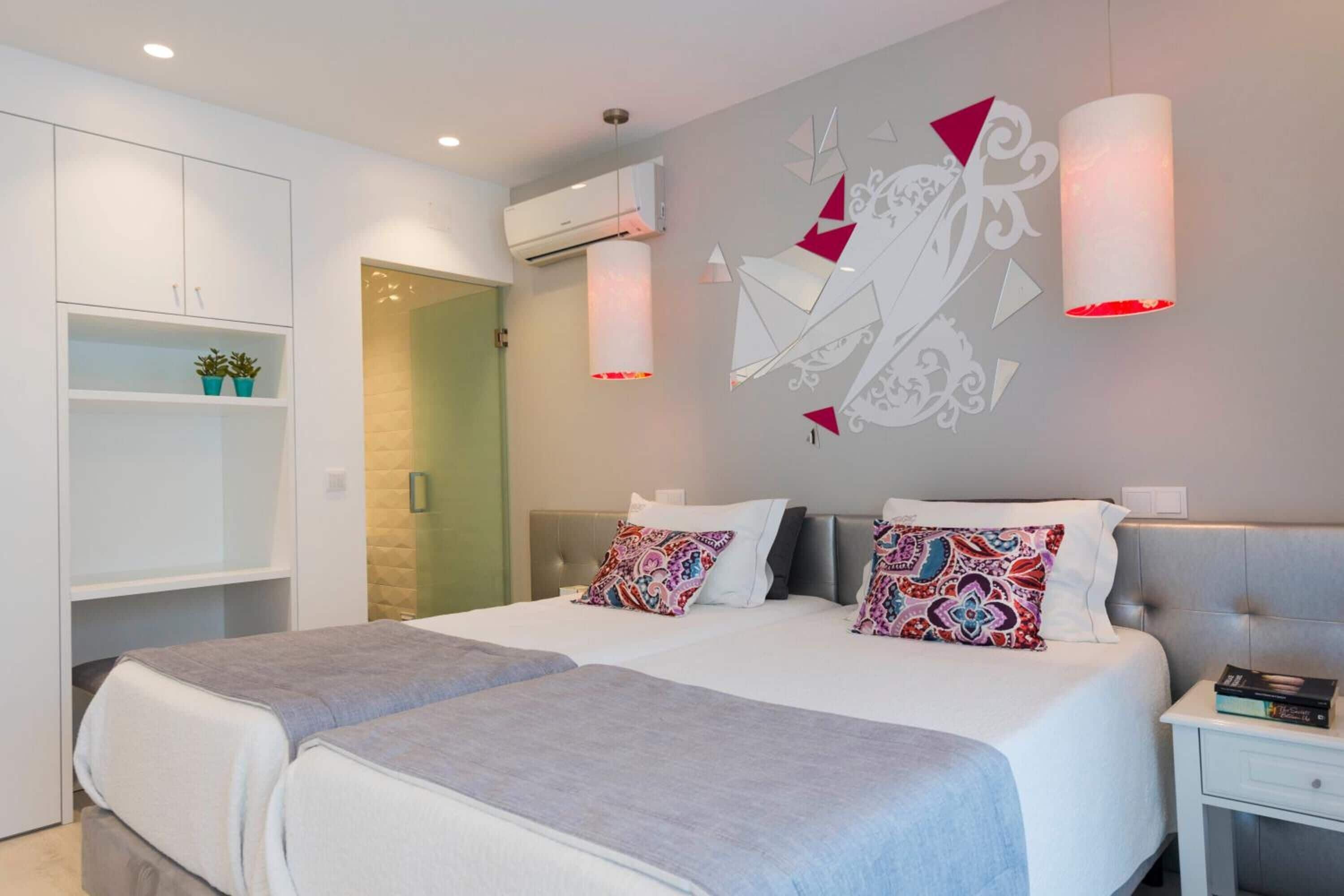 Quarto moderno com cama de casal, duas mesas de cabeceira, um guarda-roupa e um objeto decorativo na parede.