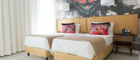 A double bed with a headboard, two bedside tables, a telephone, and a wall with floral artwork.