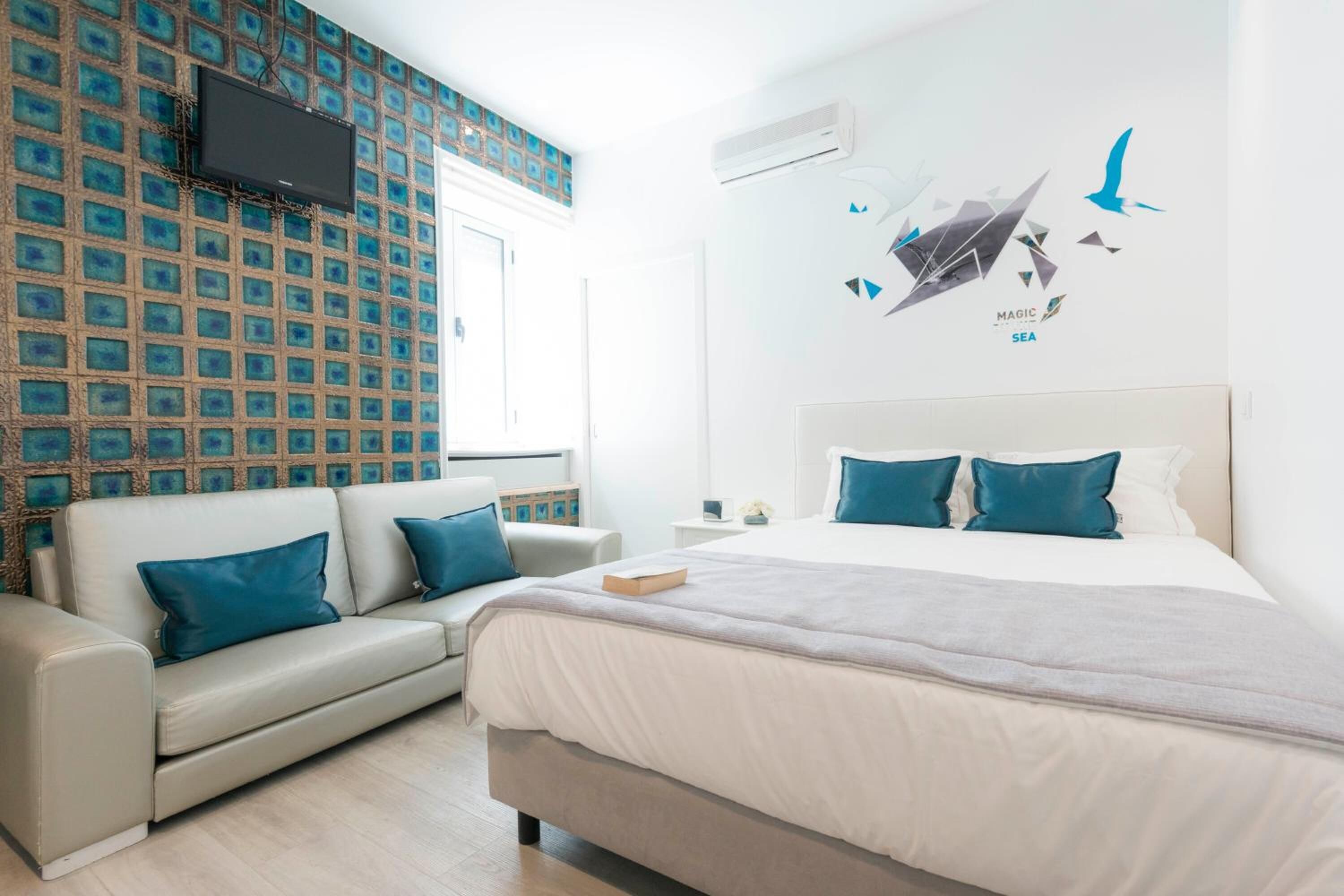 A modern hotel room with a large bed, a sofa, and a wall-mounted TV.