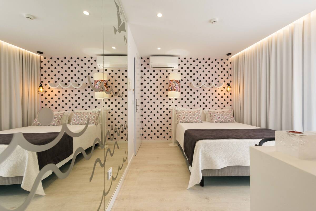 A modern hotel room with two beds, a glass partition, and patterned walls.