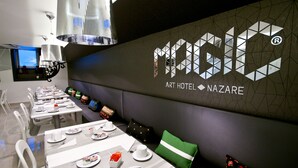 Un espace de restauration moderne dans un hôtel, avec des tables préparées pour le petit-déjeuner, une grande œuvre d’art géométrique sur un mur et une vue sur la ville par une fenêtre.