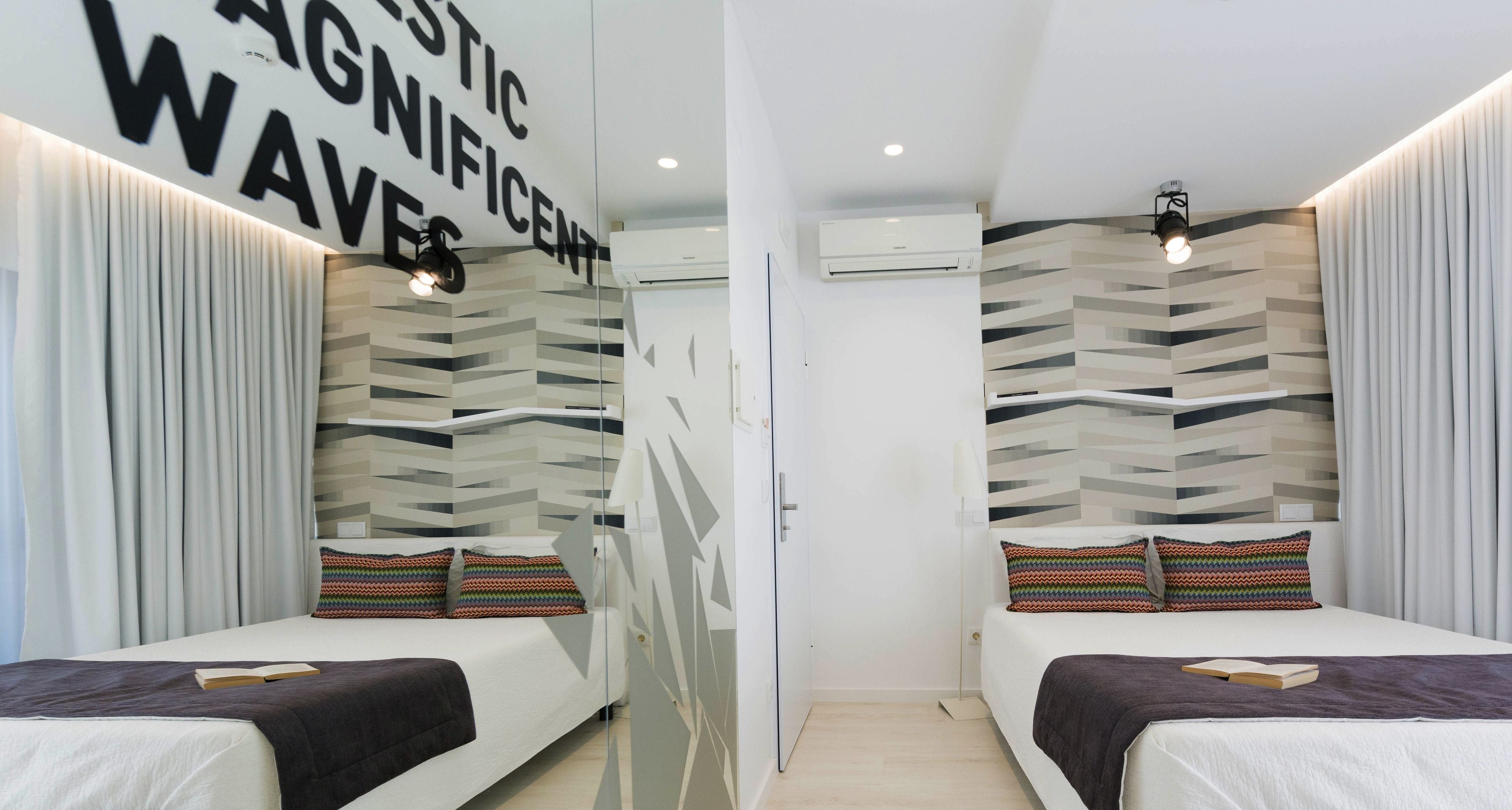 A modern hotel room with two beds, a geometric patterned wall, and an air conditioning unit.