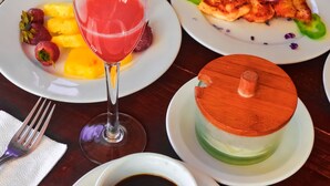 A dining table with plates of food, a glass of red drink, a cup of black coffee, and a dessert with a wooden lid.