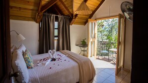A bedroom with a bed, a bedside table, a fan, and a view of the outdoors.