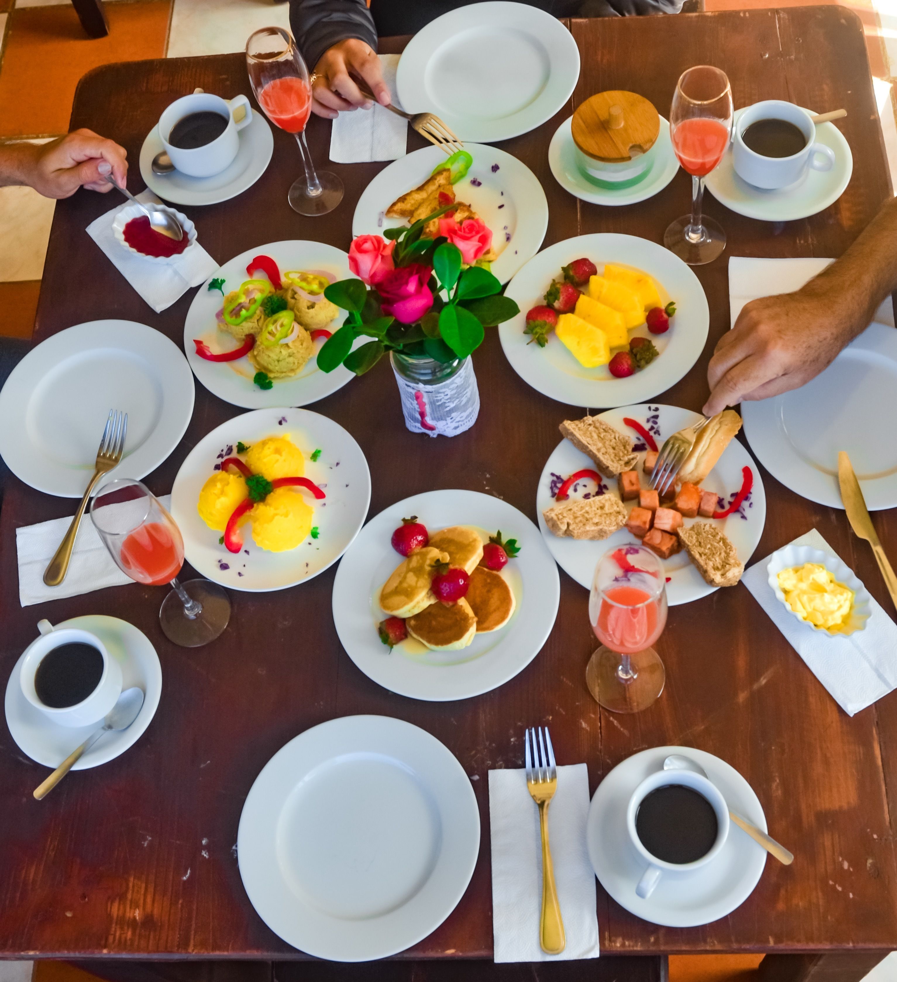 Une table en bois dressée pour le petit-déjeuner, avec différents plats, boissons et ustensiles.